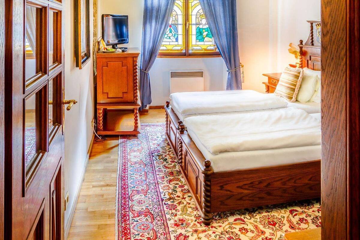 A bedroom with a large bed, a wooden dresser, a television, and a window with blue curtains.