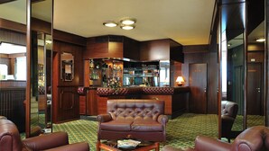 Een bar met een leren fauteuil, een bijzettafeltje en een kamerbreed tapijt met een patroon.