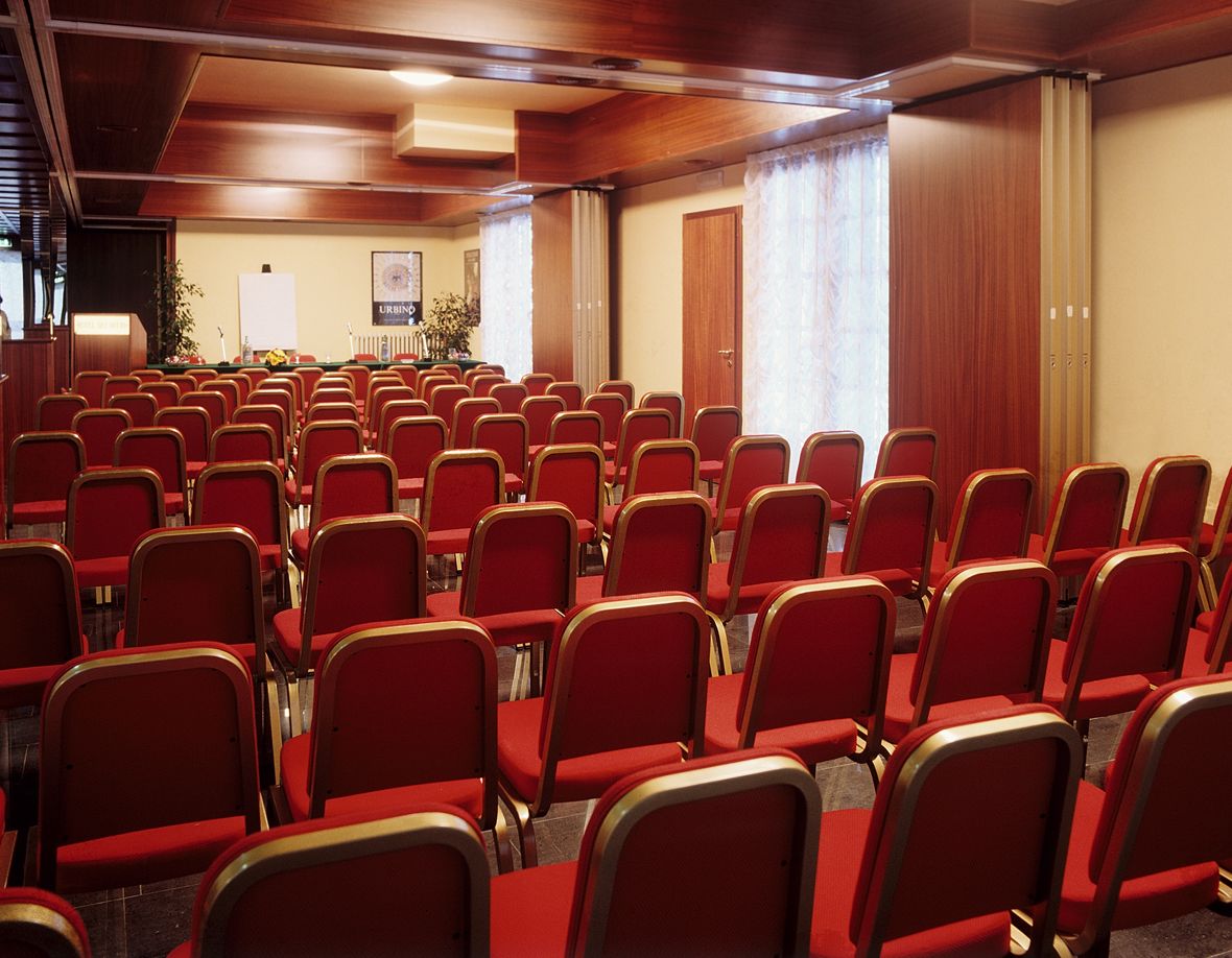 Un salón de conferencias con filas de sillas rojas y un atril al frente.