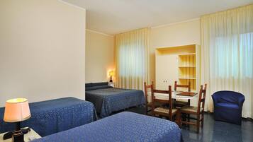 A hotel room with two beds, a desk, a chair, and a small table.