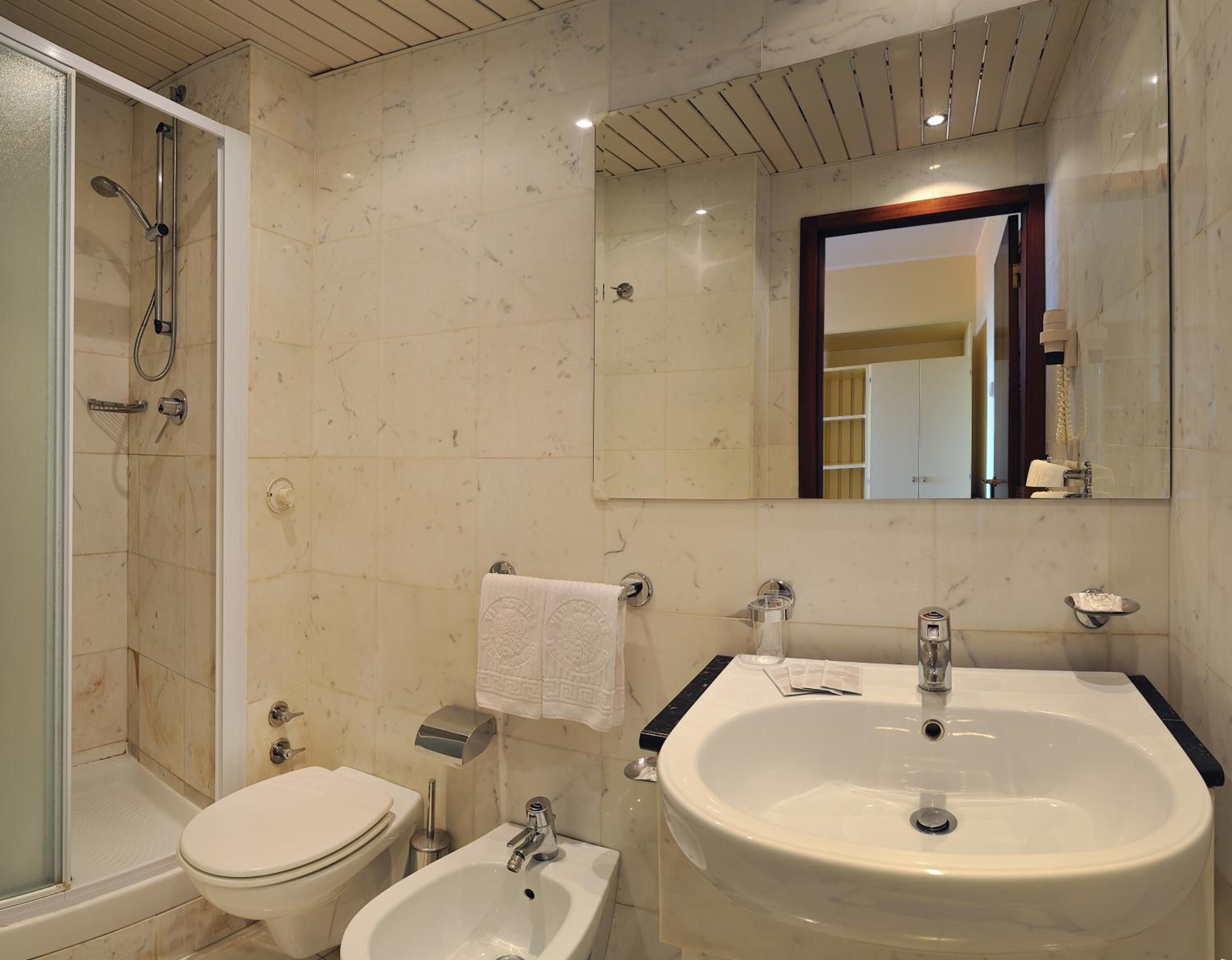 Een badkamer met douche, toilet, bidet, wastafel en spiegel.
