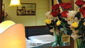 Hotelkamer met een ontbijtarrangement, waaronder een tafel met een lamp, een vaas met bloemen en een dienblad met croissants, koffie en sap.