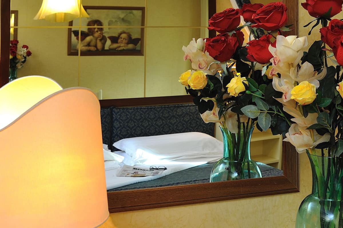 Ein Hotelzimmer mit Frühstücksecke, inklusive Tisch mit Lampe, Blumen in einer Vase und einem Tablett mit Croissants, Kaffee und Saft.
