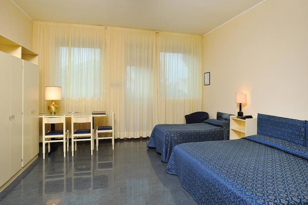 Ein Hotelzimmer mit zwei Betten, einem Schreibtisch mit Stuhl, einer Lampe und einem Kleiderschrank.