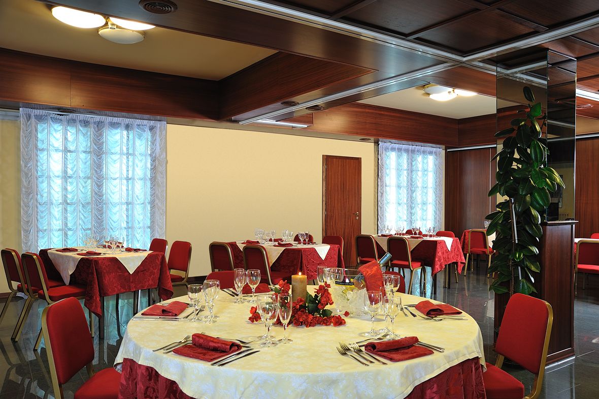 A dining area with round tables set for a meal, red chairs, and a large potted plant.