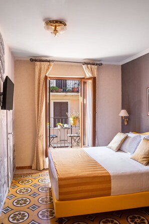 Habitación de hotel con cama, televisor, balcón con mesa y sillas, y vista a la calle.