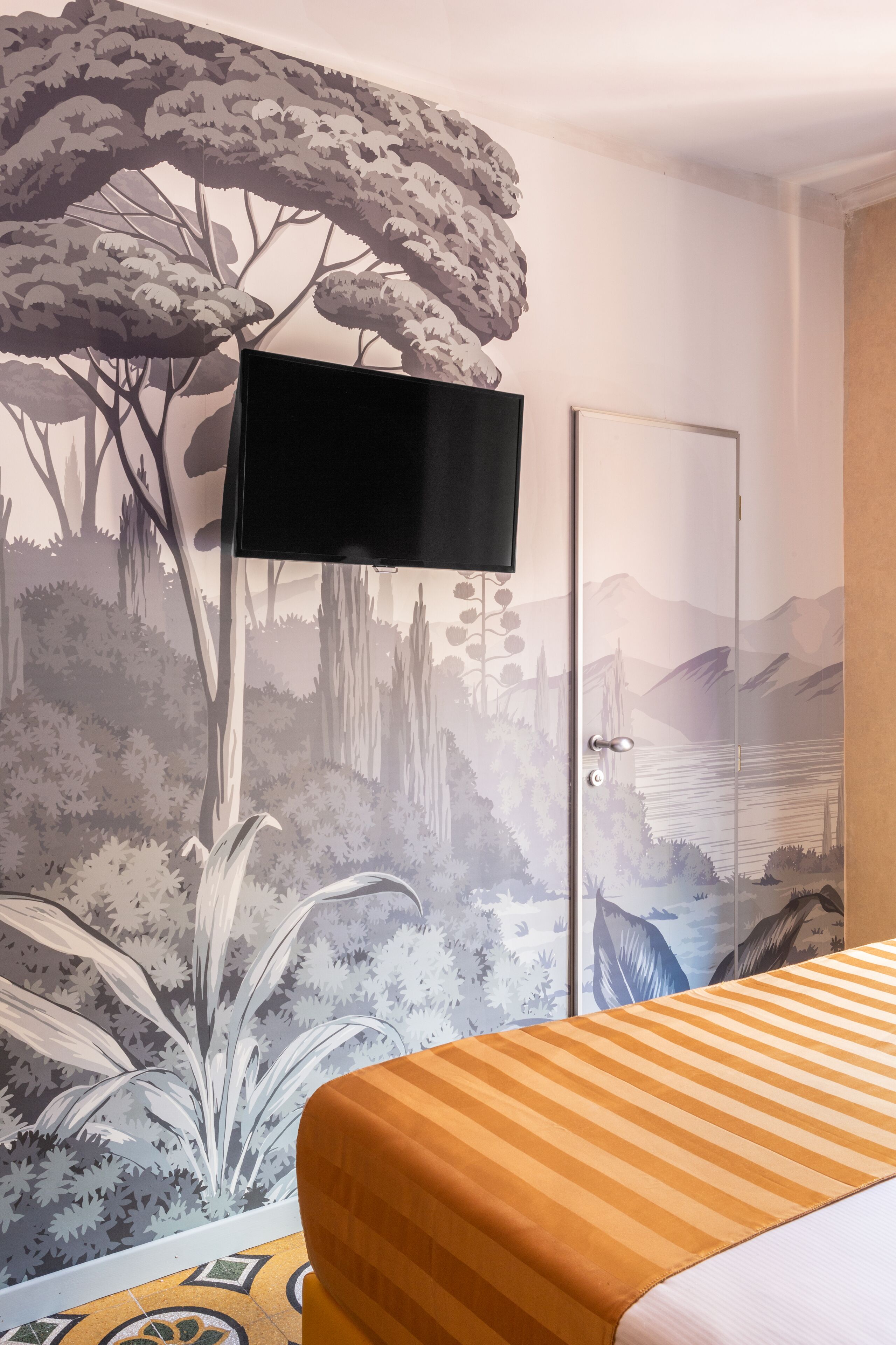Une chambre à coucher ornée d’une fresque représentant une scène de forêt, un lit avec une literie à rayures et une porte donnant sur une vue sur les montagnes.