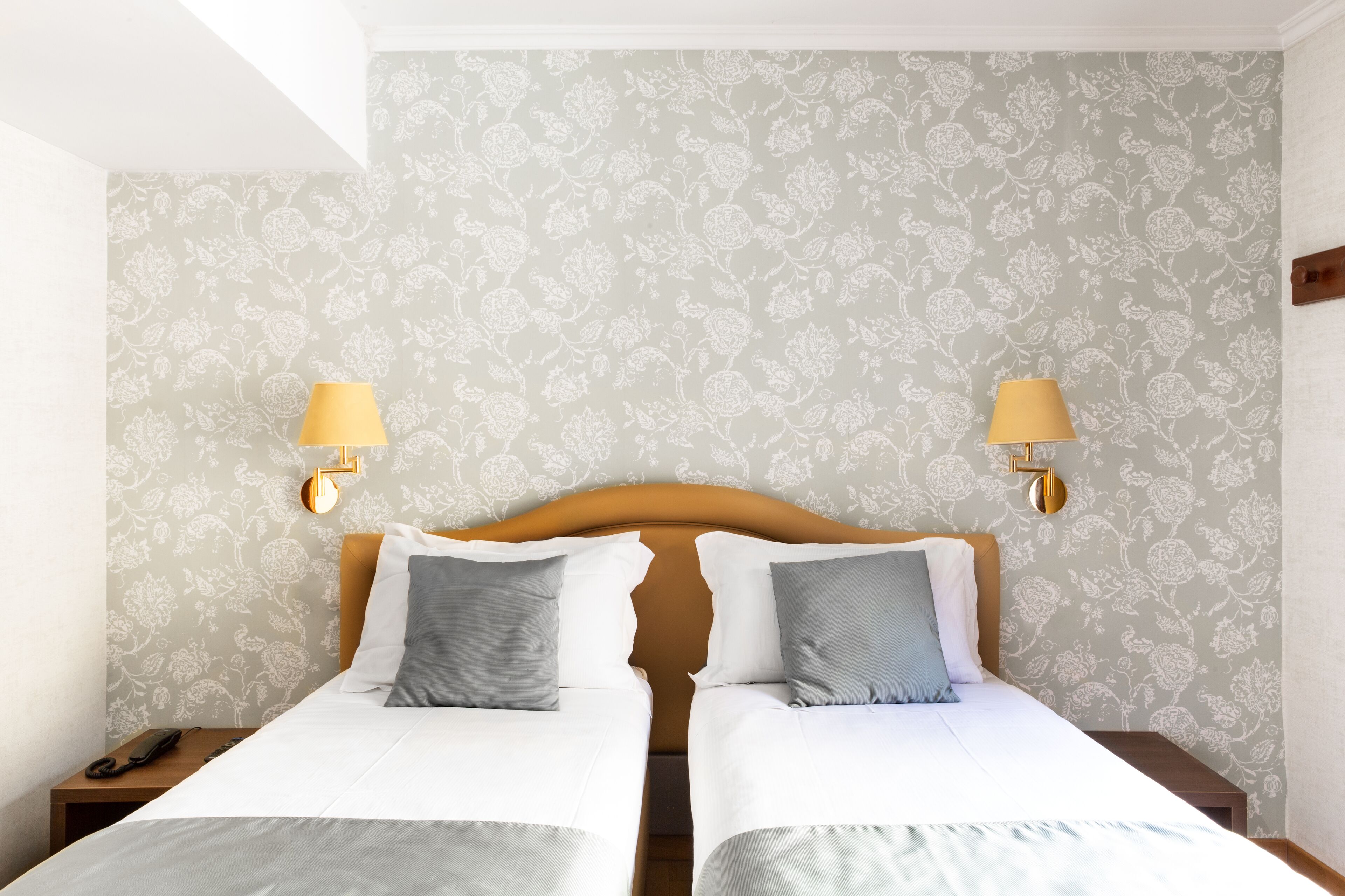 A hotel room with two beds, a wooden headboard, and a floral wallpaper pattern.