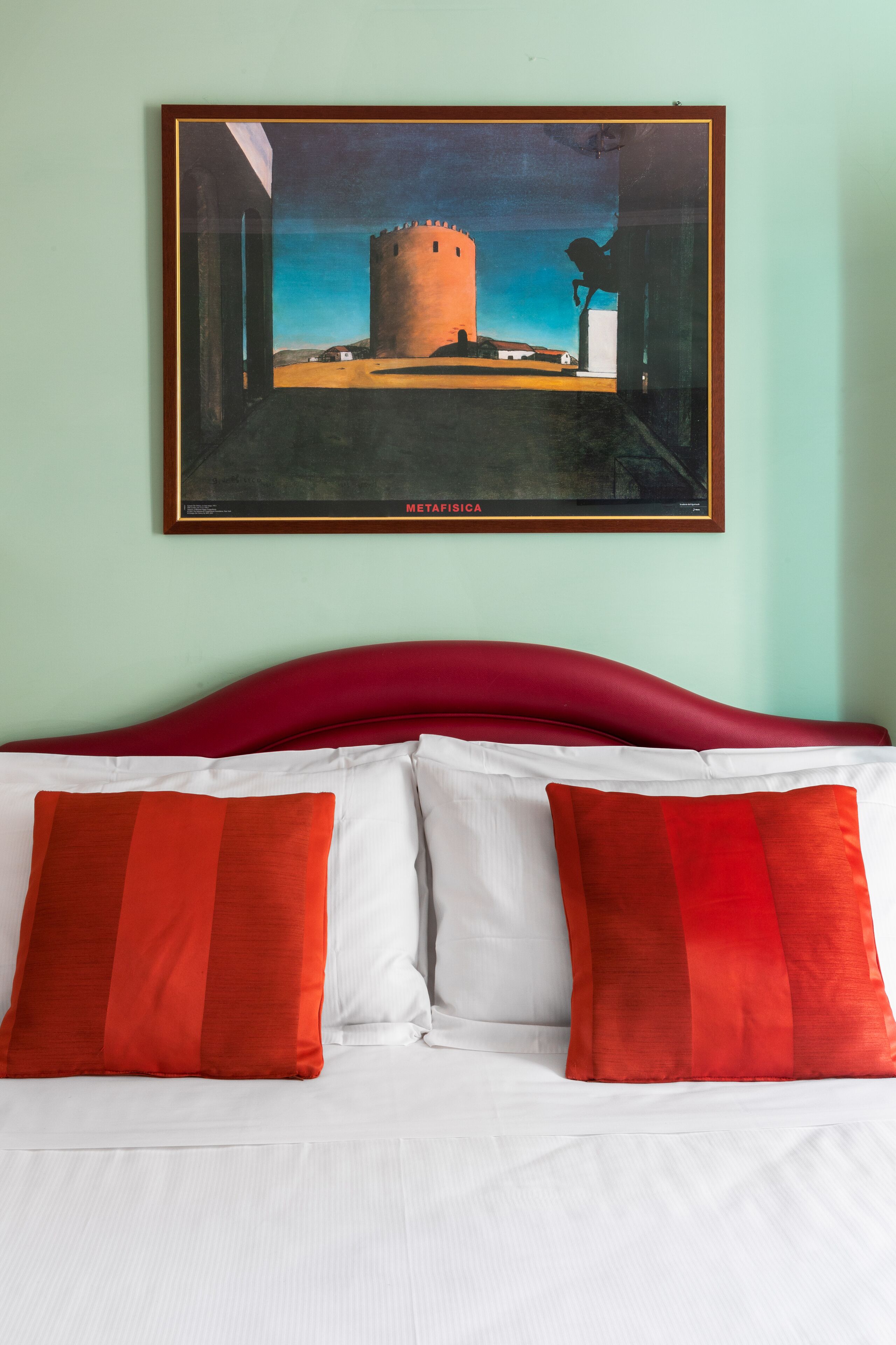 Un lit avec une literie blanche et rouge, une tête de lit rouge et un tableau encadré représentant un château accroché au mur.