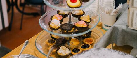 A dessert display with various cupcakes and fruit bowls on a wooden table.