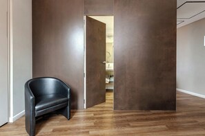 A modern interior with a black leather chair, a wooden floor, and a partially open door leading to another room. - Al Manthia Hotel - Trevi Hotels Group (Rome)