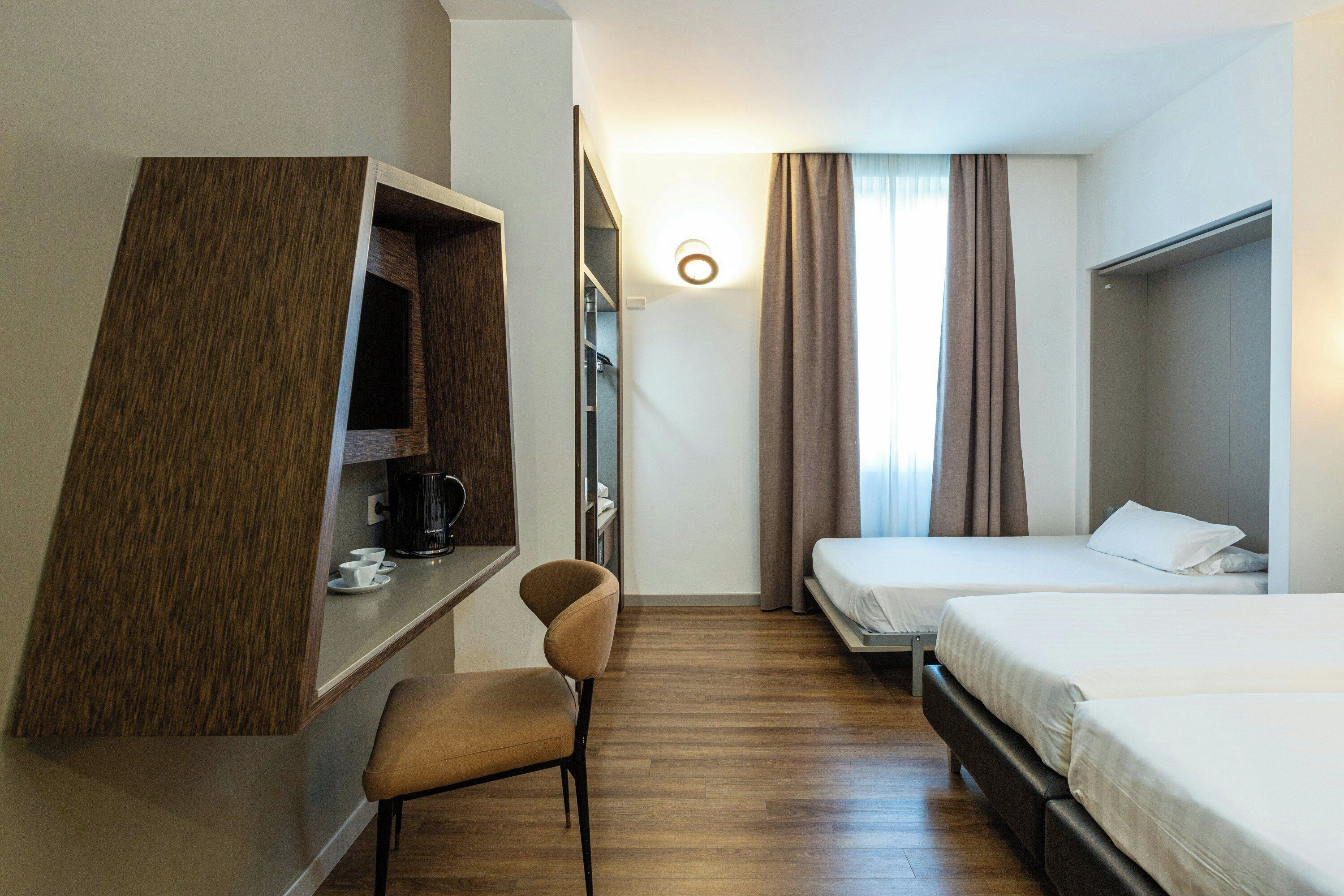 A hotel room with a desk, chair, two beds, and a wardrobe.