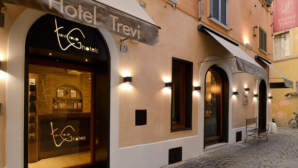 Hotel Trevi, Fassade mit Kopfsteinpflasterstraße, beleuchteter Beschilderung und einem Fahrrad vor dem Haus.