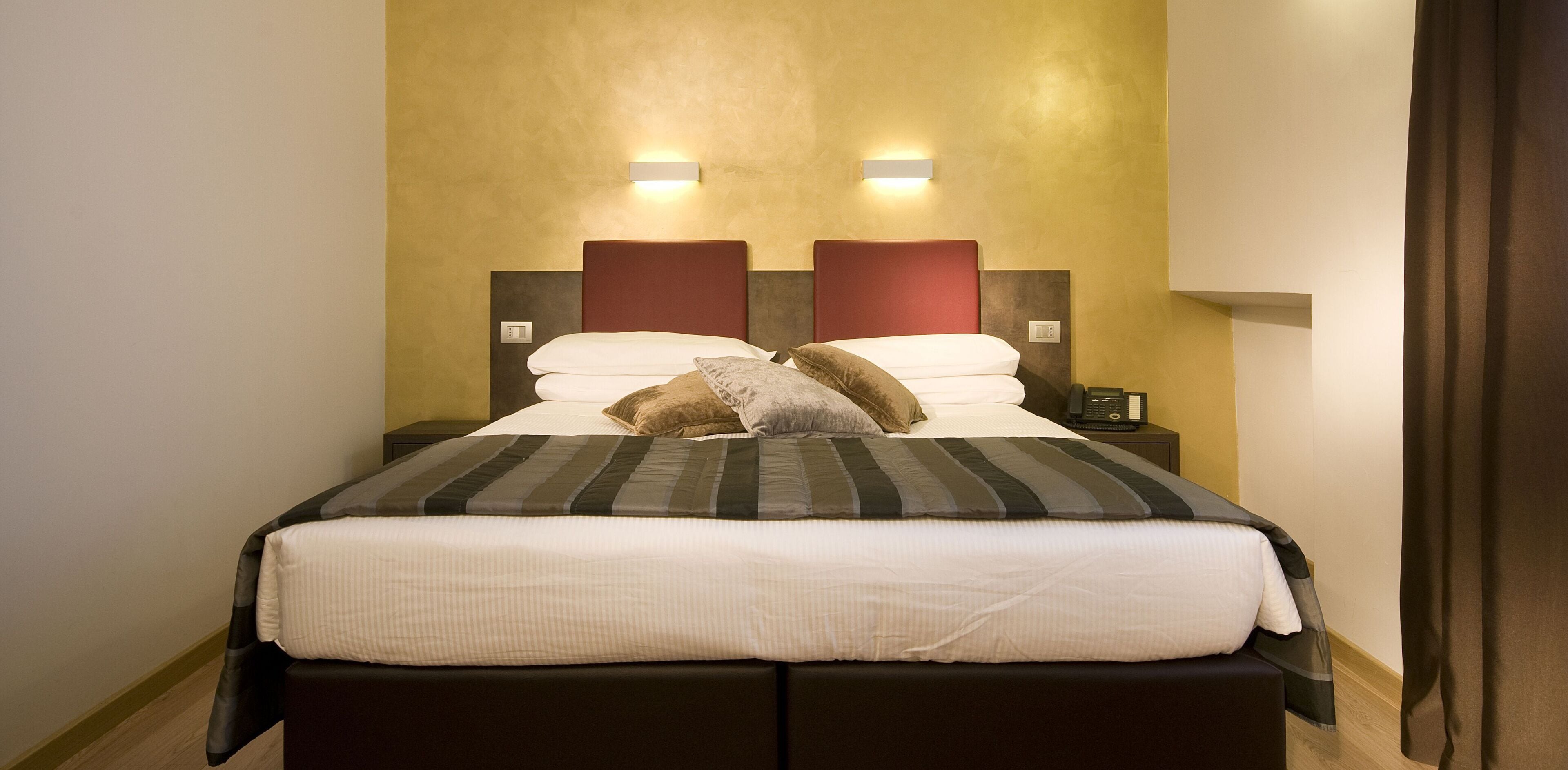 A double bed with a striped bedspread, two wall-mounted light fixtures, and a bedside table with a phone.