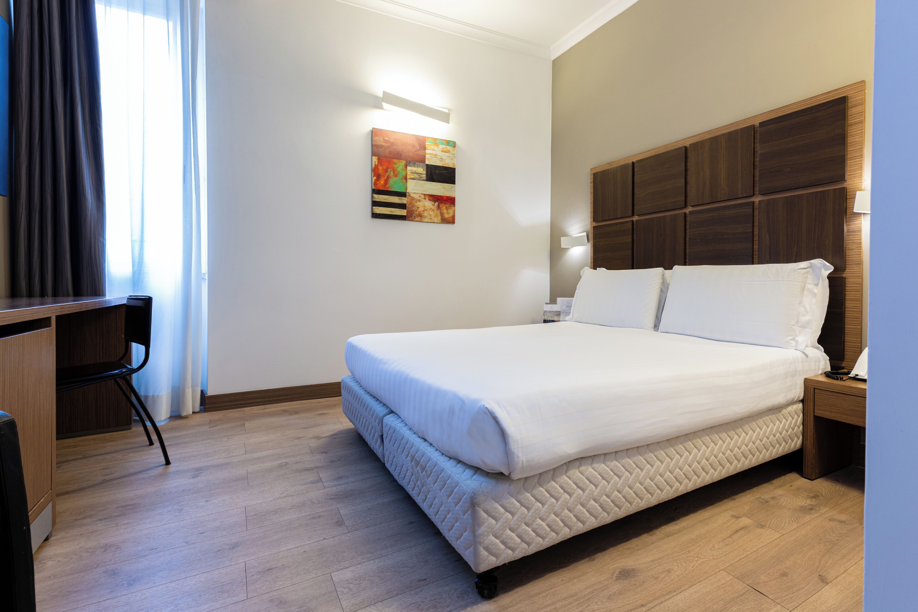 A hotel room with a bed, a desk, and a wall-mounted artwork.