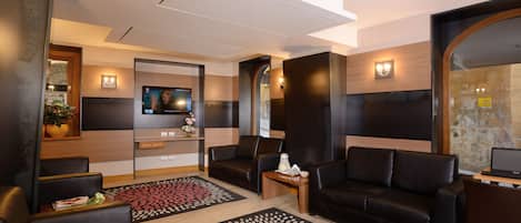 Un hall d’hôtel moderne avec des canapés en cuir, un téléviseur à écran plat et un tapis à motifs.