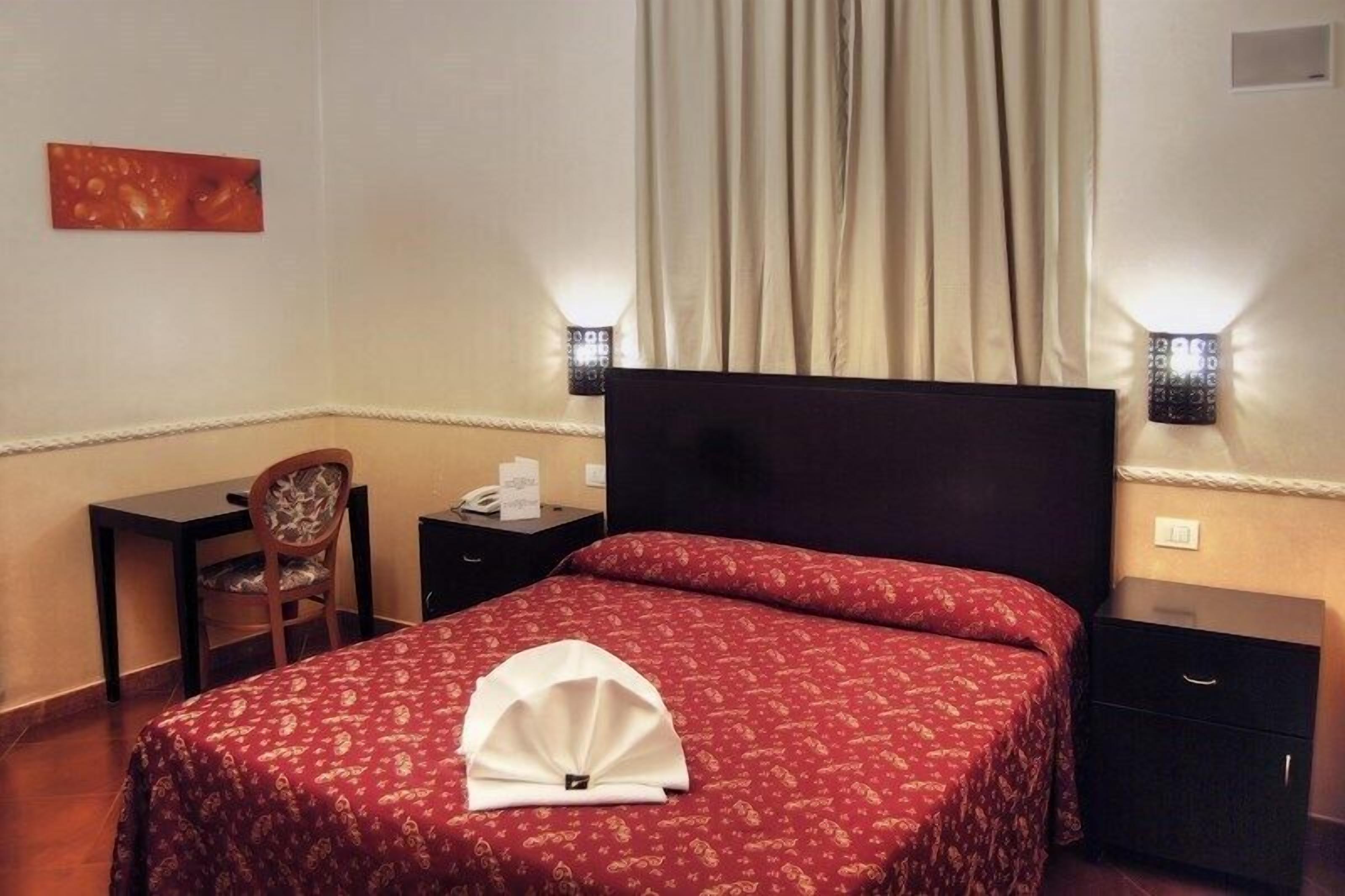 A hotel room with a bed, bedside tables, a desk, and a chair.