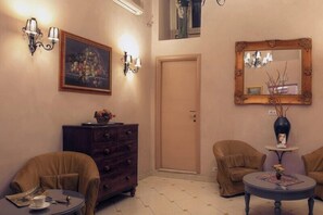 A room with a wooden door, a dark wooden dresser, two brown armchairs, a round coffee table, a framed mirror, and wall-mounted sconces. - Hotel Picasso (Rome)