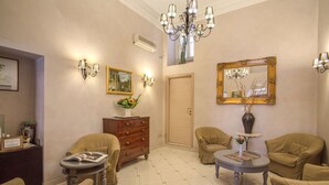 Um quarto com paredes bege, um candelabro, um espelho grande e duas poltronas.