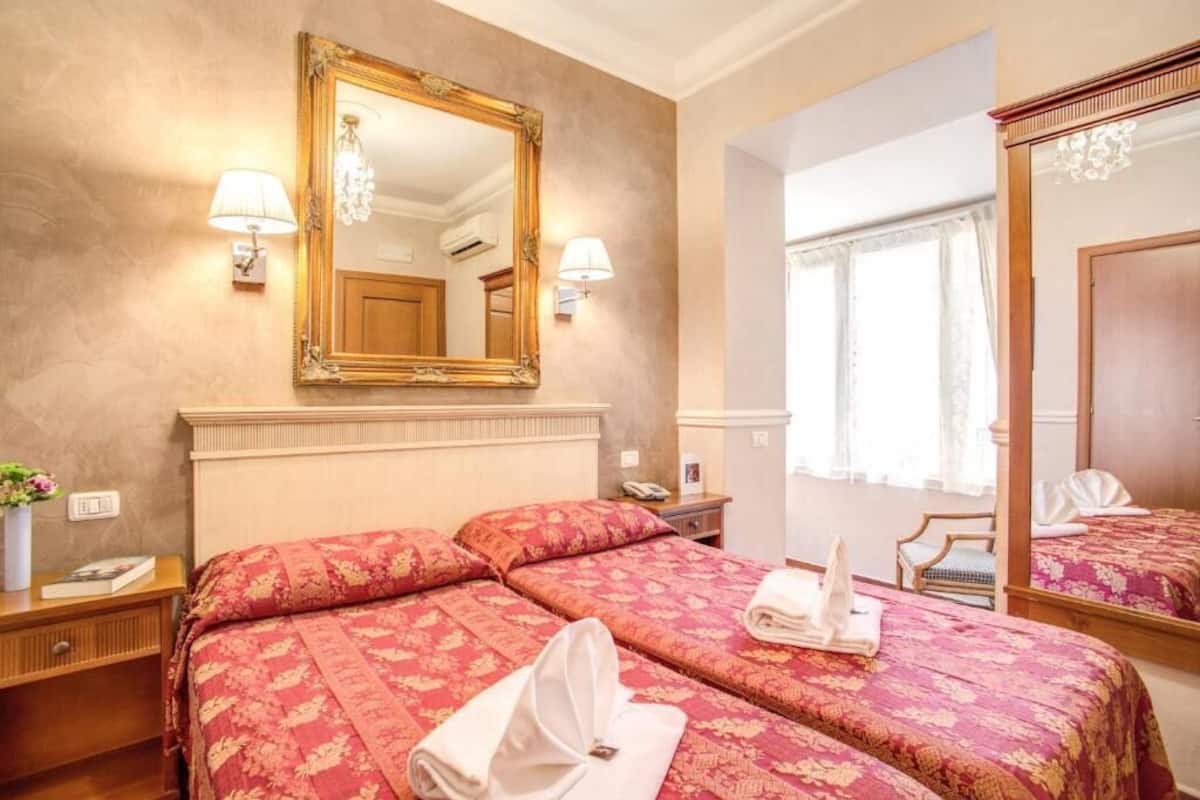 A hotel room with a large bed, two bedside tables, a mirror, and a window with curtains.
