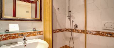 Casa de banho com lavatório, espelho, chuveiro e azulejos decorativos.