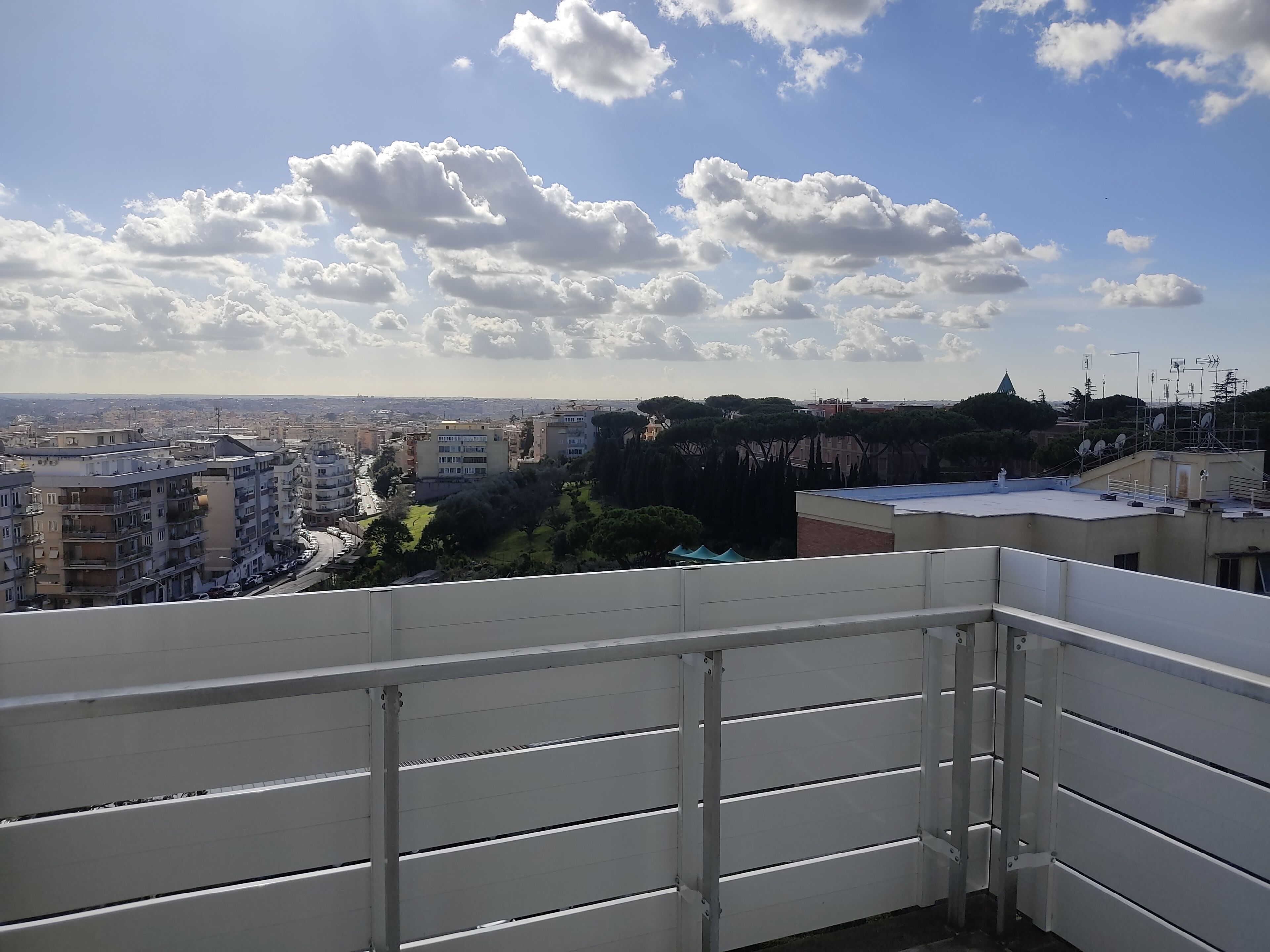 A balcony with a view of a cityscape, including buildings and trees.
