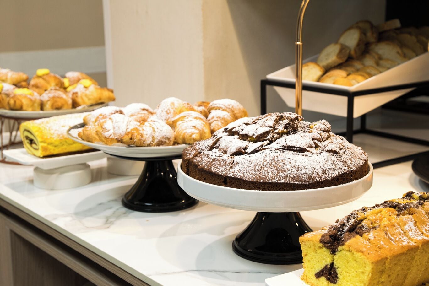 A buffet with various baked goods including pastries, a chocolate cake, and a yellow cake.