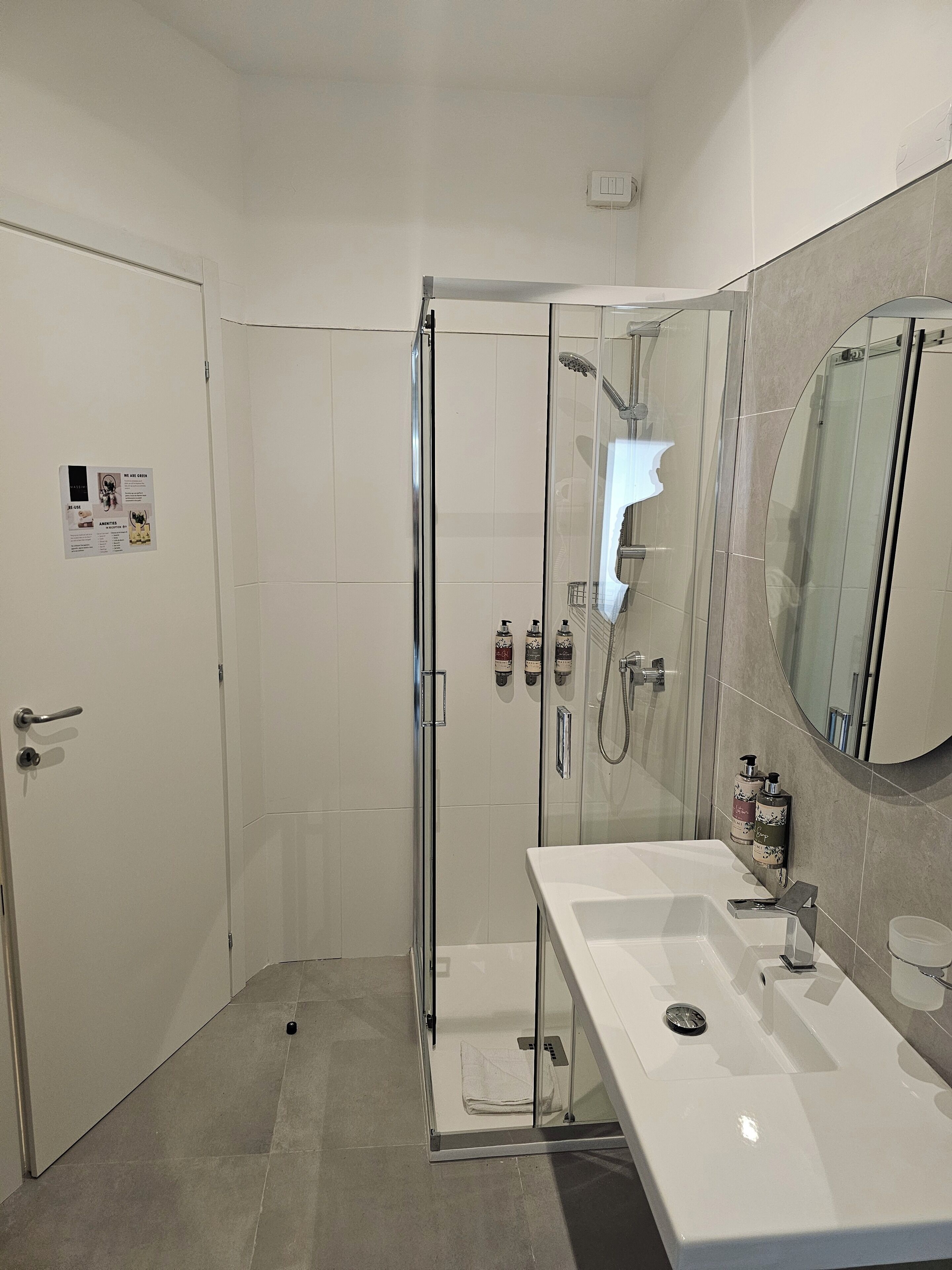 A modern bathroom with a glass-enclosed shower, a white sink with a mirror, and a door with a sign.