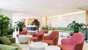 Un vestíbulo moderno con asientos verdes y rosados, un mostrador de recepción y plantas en macetas.