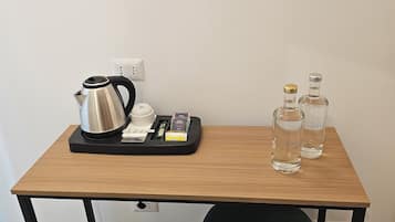 Uma pequena mesa de madeira com uma chaleira, um tabuleiro com livros e uma caneta, e duas garrafas.