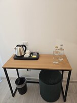A small wooden table with a kettle, a tray with books and a pen, and two bottles on it.