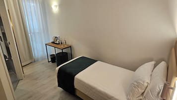 Habitación de hotel con cama, mesita de noche con teléfono, una pequeña mesa con tetera y tazas, y ventana con cortinas.