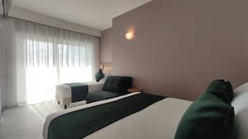 Una habitación de hotel moderna con una cama grande, un sofá, una mesita y una ventana con cortinas de gasa.
