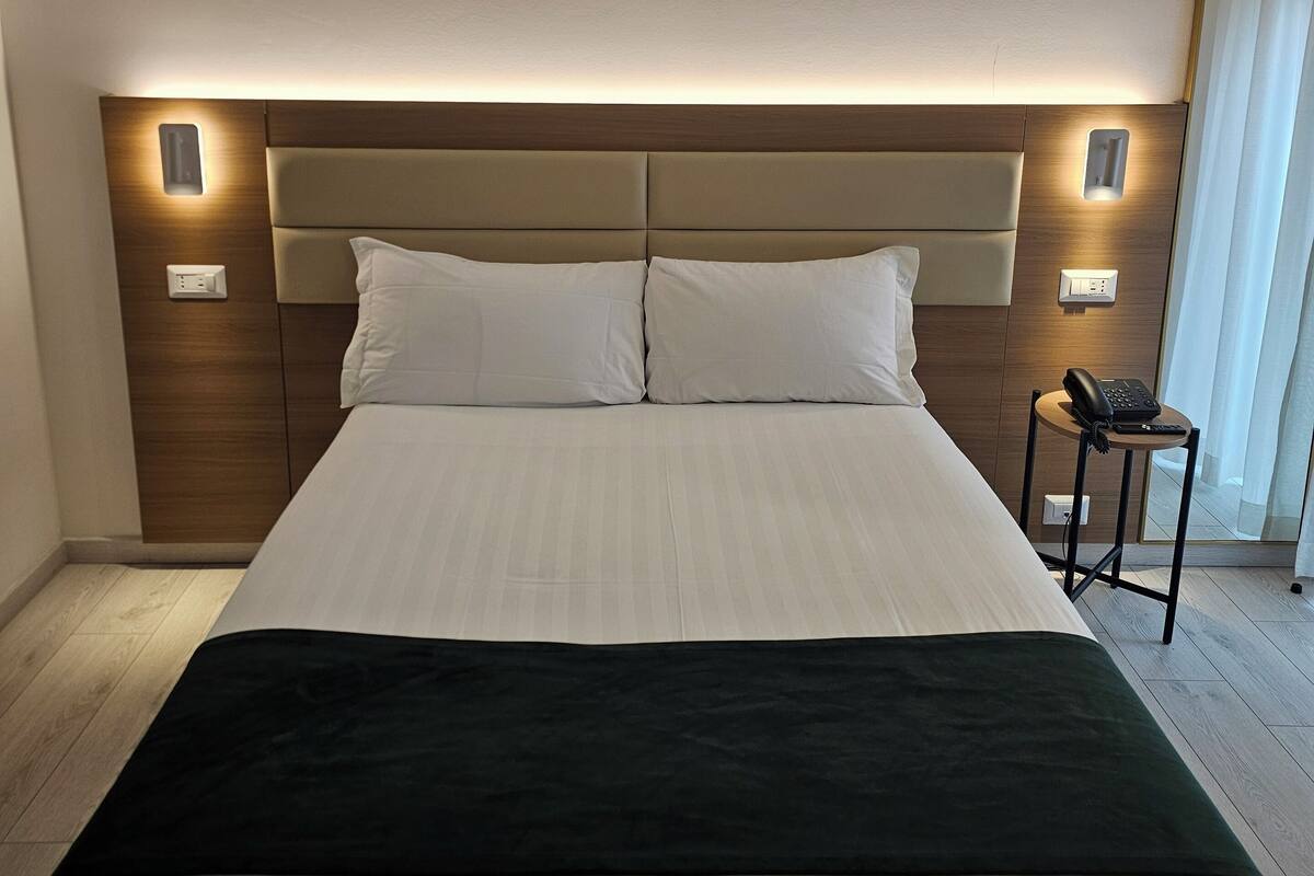 Ein Hotelzimmer mit einem großen Bett, einem Nachttisch mit Telefon und Wandlampen.