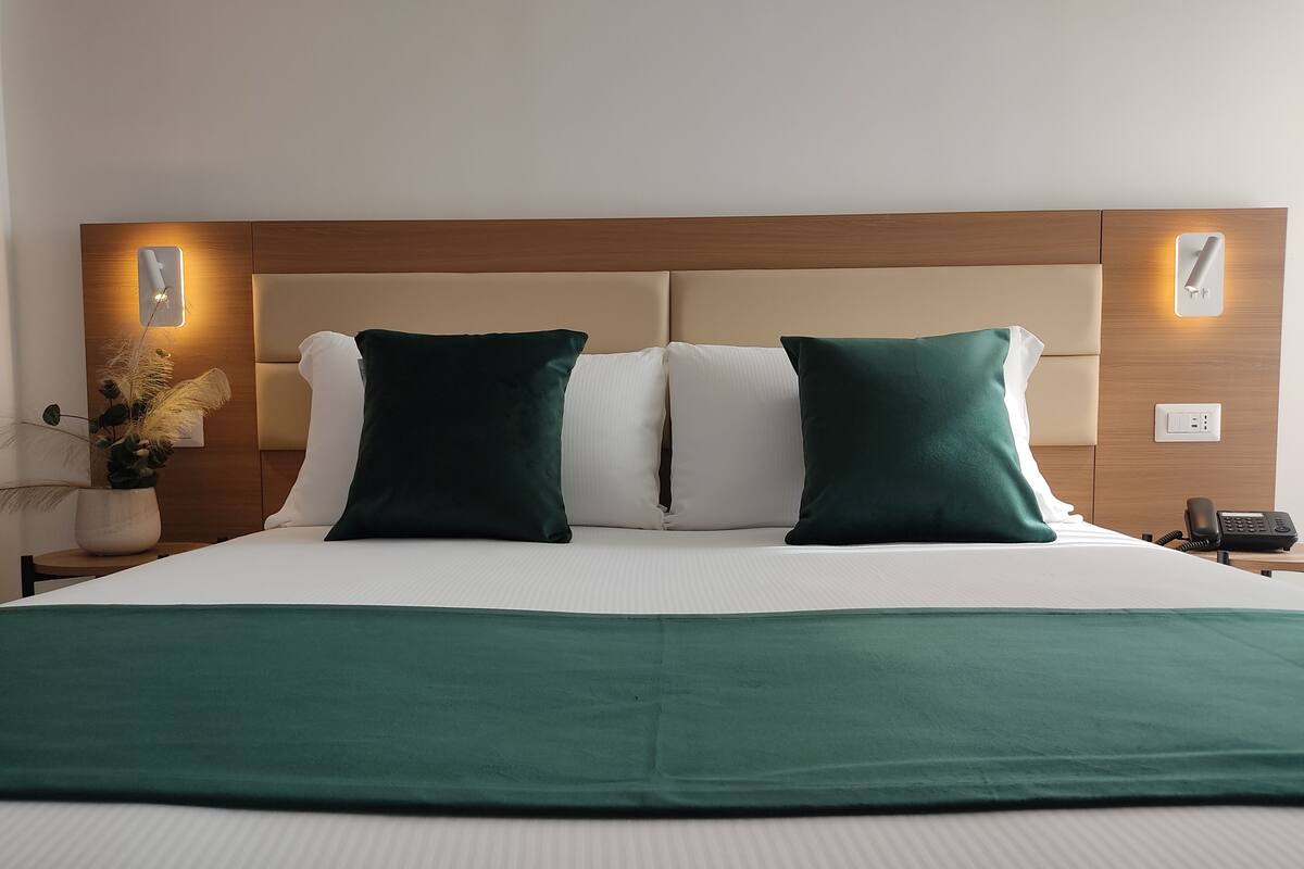 Ein Hotelzimmer mit einem großen Bett, zwei Kissen, einem Nachttisch mit Telefon und einer Wandleuchte.