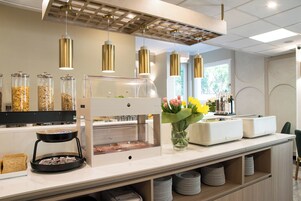 A modern breakfast bar with a glass display case, a coffee station, and a vase of flowers.