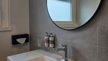 Un baño con un lavamanos blanco, un espejo redondo y dos botellas de jabón en la pared.