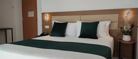 Una camera d'albergo con un letto, comodini, una lampada a muro e una porta.