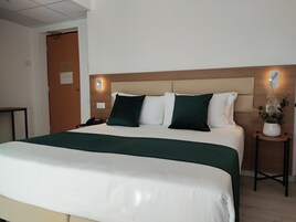 Una camera d'albergo con un letto, comodini, una lampada a muro e una porta.