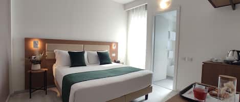 A neatly arranged hotel room with a large bed, bedside table, and a small table with a tray of breakfast items.