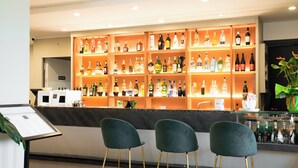 Zona de bar con estantes llenos de botellas de licores, una barra y tres taburetes verdes.