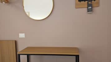 Una habitación con un espejo redondo, una mesa de madera, un reposapiés verde y un cubo de basura negro.