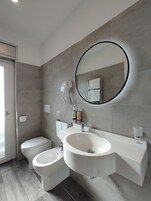 Ein modernes Badezimmer mit Toilette, Bidet und einem großen Waschbecken mit Spiegel darüber.