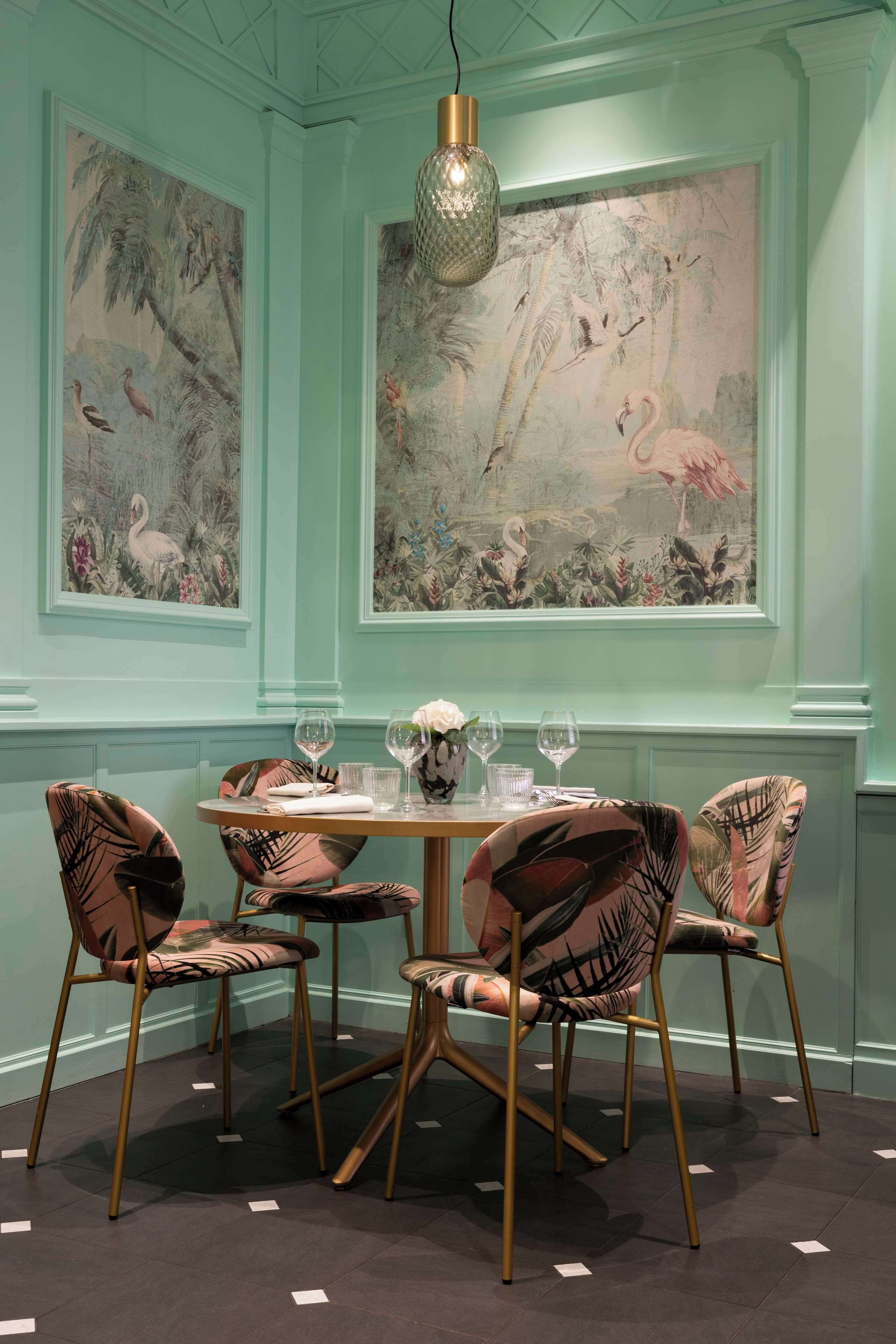 A dining area with a round table, four chairs, and two large wall paintings of tropical scenes.