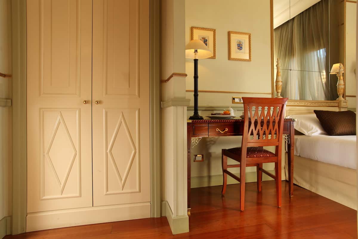 A room with a wooden desk, a chair, a bed, and a large mirror.