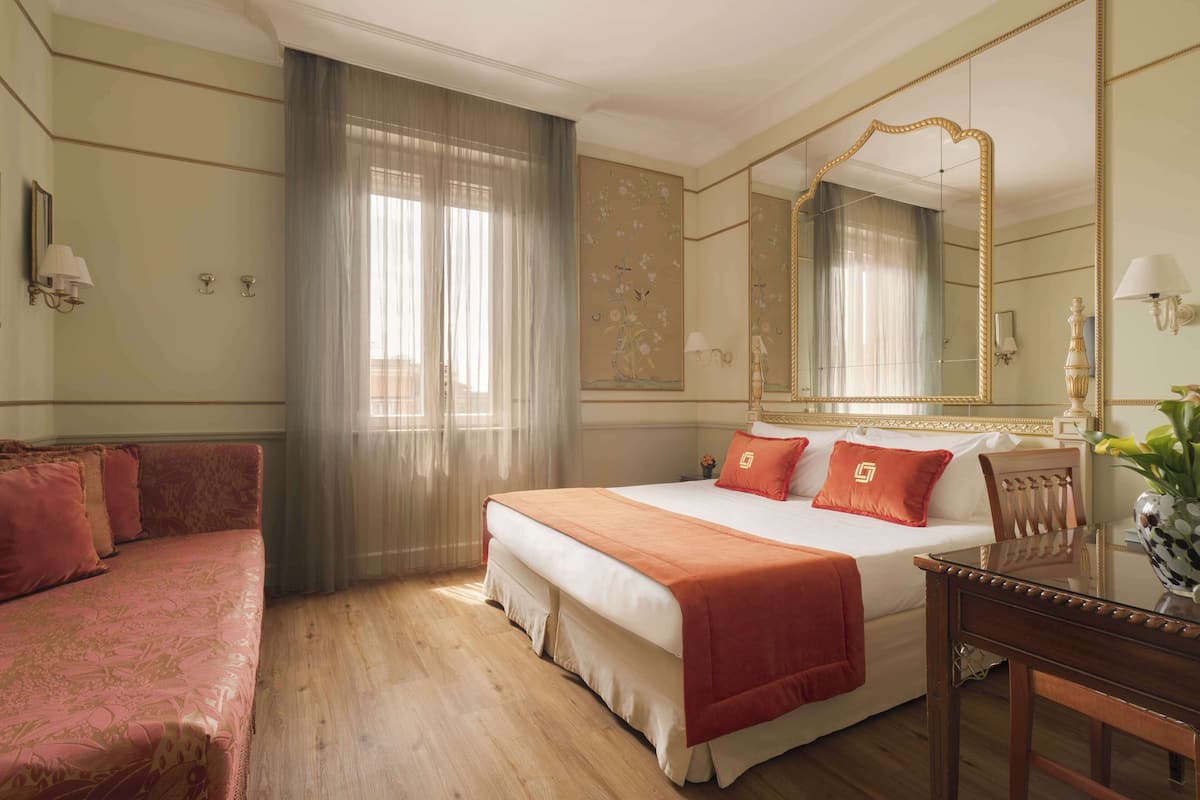 A hotel room with a large bed, a sitting area with a sofa, a wooden table, and a large mirror.
