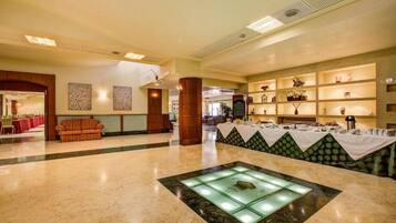 A spacious lobby with a marble floor, a central glass display, and a buffet area with a green patterned tablecloth.