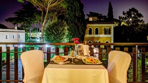 A table set for two with a view of a building and trees at night. - Appia Park Hotel (Rome)