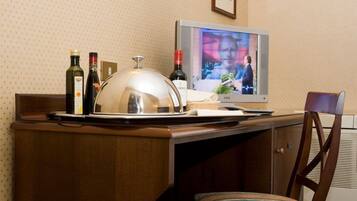 A hotel room with a wooden desk, a covered food trolley, a television, and a chair.