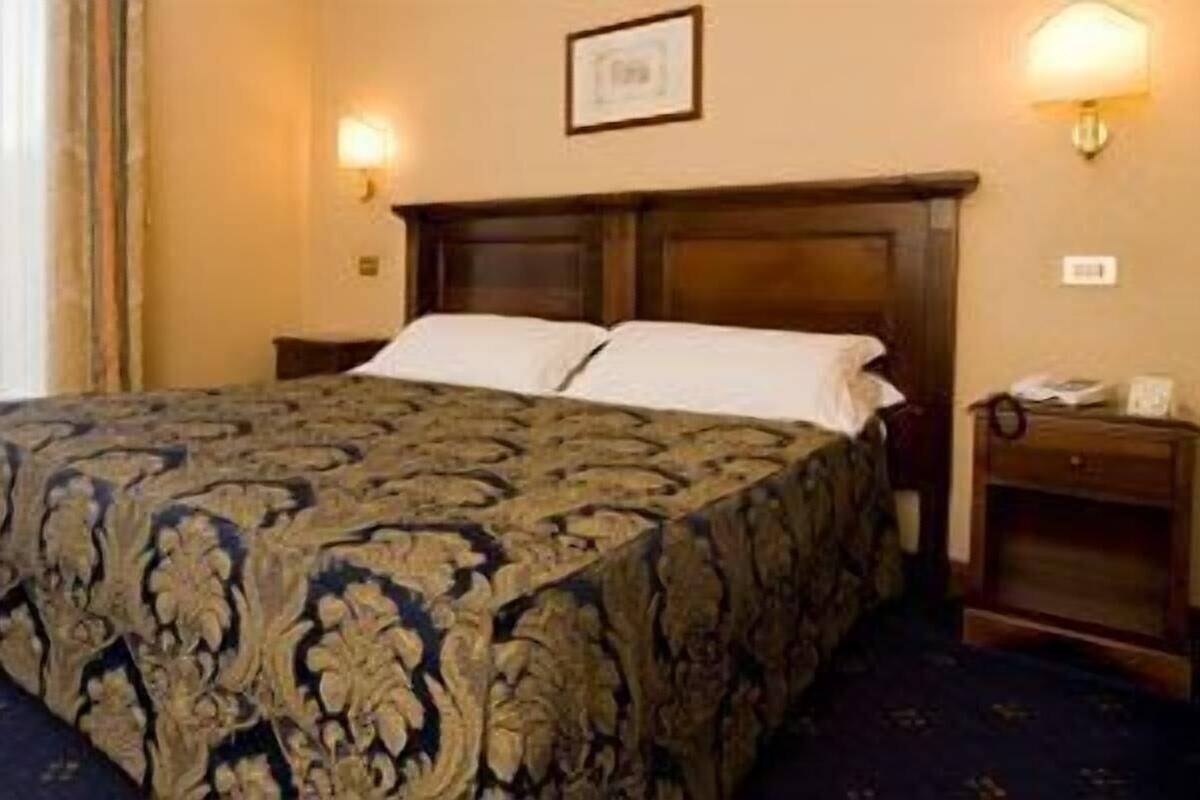 A hotel room with a large bed, two bedside tables, a nightstand, and a framed picture on the wall.